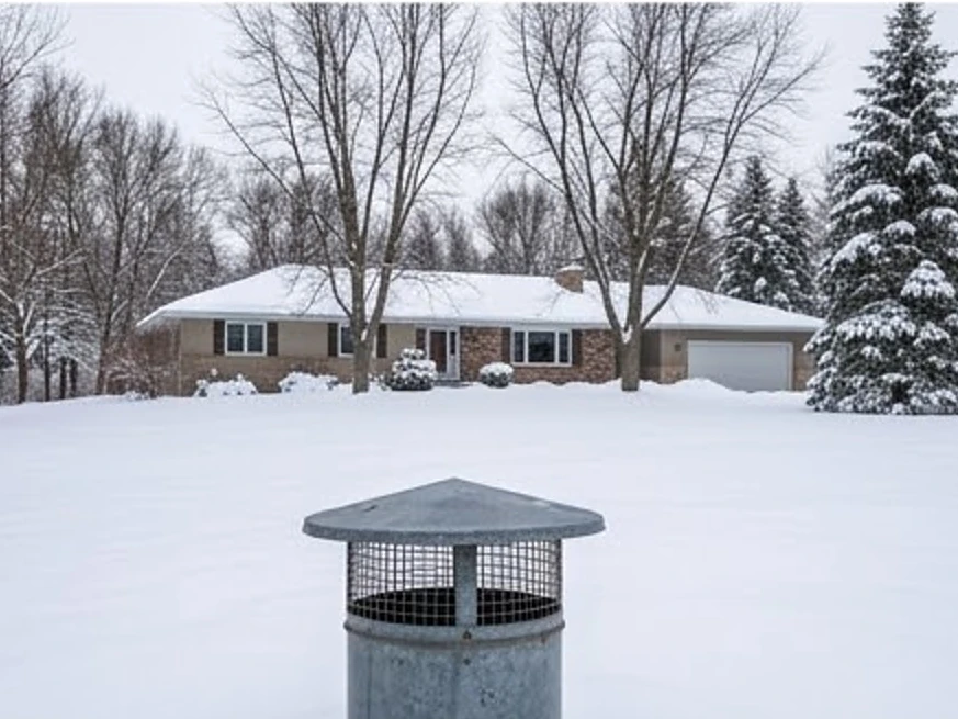 Well cap in the foreground, ranch home on acreage behind it on the edge of the Twin Cities suburbs in winter snow (Washington County, Minnesota)