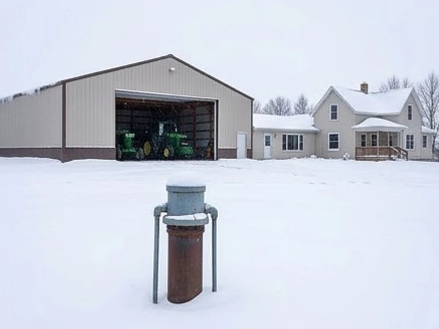 Mendota Heights, MN water testing: well cap in the foreground, machine shed and farmhouse behind it in rural Minnesota in winter snow